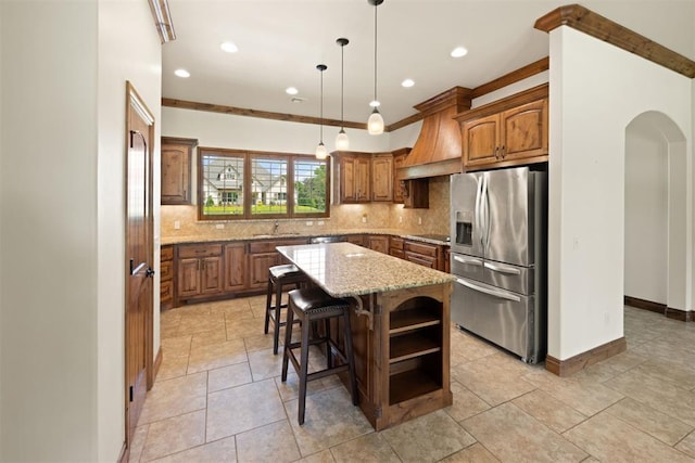 kitchen featuring stainless steel refrigerator with ice dispenser, decorative backsplash, custom exhaust hood, and a center island