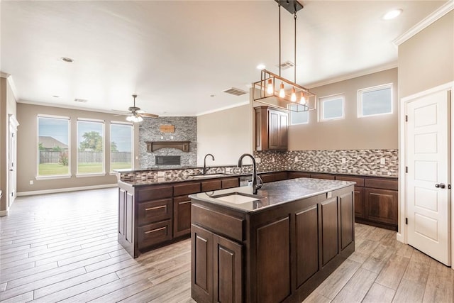 kitchen with an island with sink, dark brown cabinets, hanging light fixtures, and sink