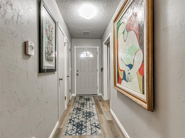 doorway with a textured ceiling and light hardwood / wood-style flooring