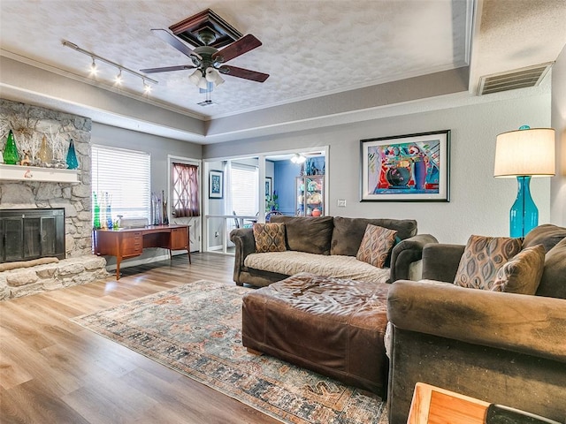 living room featuring ceiling fan, ornamental molding, track lighting, wood-type flooring, and a stone fireplace