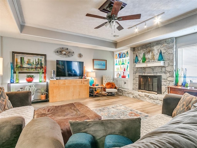 living room featuring track lighting, a raised ceiling, hardwood / wood-style floors, a fireplace, and ornamental molding