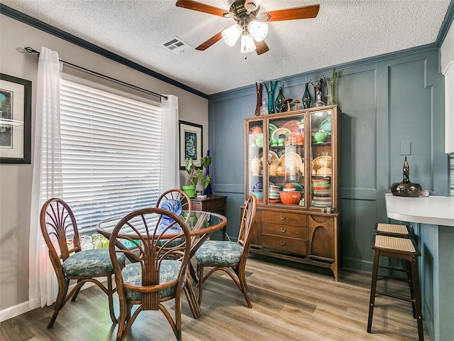 dining room with a textured ceiling, ceiling fan, crown molding, and wood-type flooring