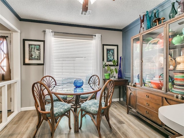 dining room with a textured ceiling, light wood-type flooring, and ornamental molding