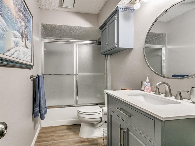 full bathroom with toilet, a textured ceiling, combined bath / shower with glass door, wood-type flooring, and vanity