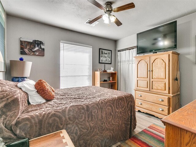 bedroom with ceiling fan, light hardwood / wood-style floors, and a textured ceiling