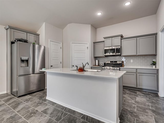 kitchen featuring a center island with sink, gray cabinetry, stainless steel appliances, sink, and tasteful backsplash