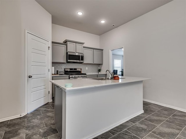 kitchen featuring stainless steel appliances, sink, tasteful backsplash, a kitchen island with sink, and gray cabinetry