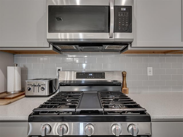 kitchen featuring stainless steel appliances, white cabinets, decorative backsplash, and light stone counters