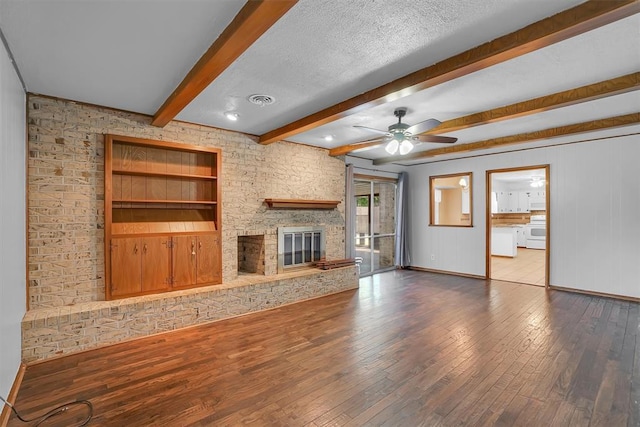 unfurnished living room with ceiling fan, hardwood / wood-style floors, beam ceiling, a stone fireplace, and a textured ceiling