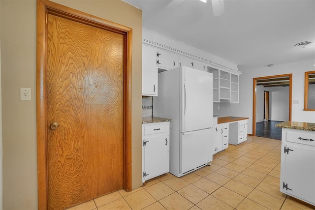 kitchen with white fridge, light tile patterned floors, white cabinetry, and stone counters