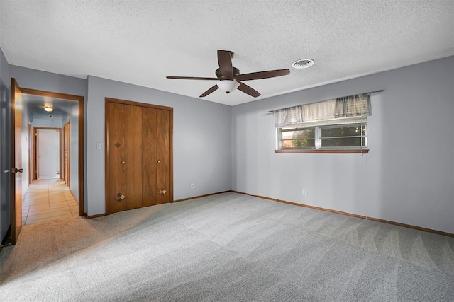 unfurnished bedroom featuring ceiling fan, light colored carpet, a textured ceiling, and a closet