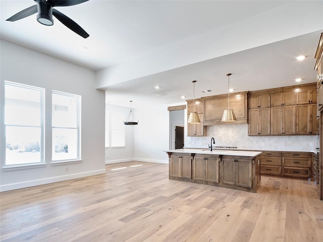 kitchen with decorative light fixtures, tasteful backsplash, a kitchen island with sink, and light hardwood / wood-style flooring