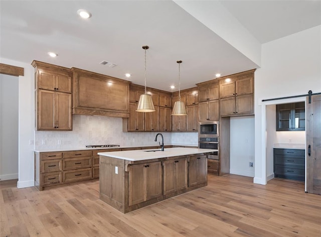 kitchen with oven, a barn door, a center island with sink, pendant lighting, and built in microwave