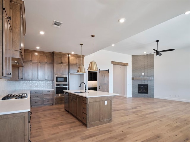 kitchen featuring a kitchen island with sink, appliances with stainless steel finishes, pendant lighting, sink, and light hardwood / wood-style flooring