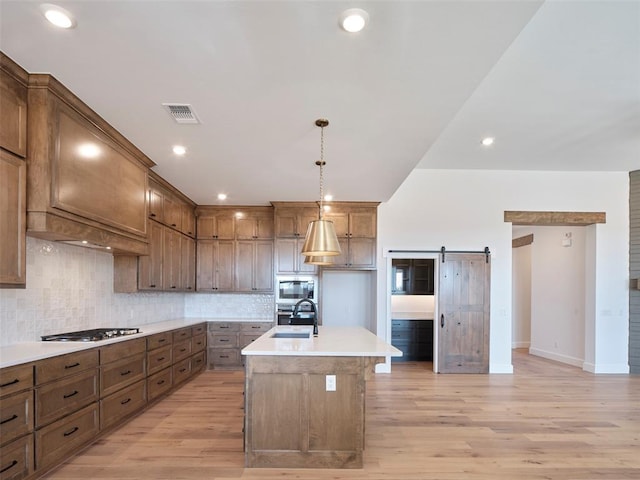 kitchen with a kitchen island with sink, a barn door, stainless steel appliances, sink, and decorative light fixtures