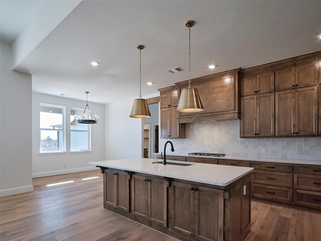 kitchen with sink, light hardwood / wood-style floors, hanging light fixtures, and an island with sink