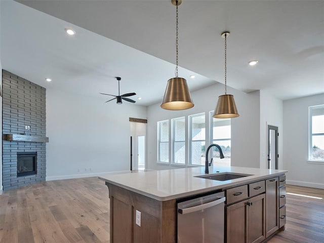 kitchen with sink, decorative light fixtures, a fireplace, dishwasher, and a kitchen island with sink