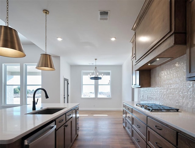 kitchen with sink, custom exhaust hood, backsplash, a center island with sink, and appliances with stainless steel finishes