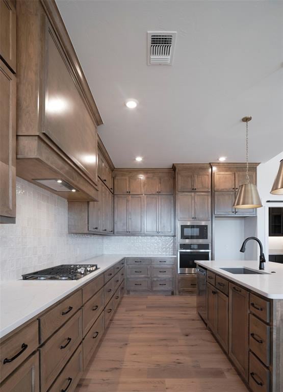 kitchen featuring pendant lighting, stainless steel appliances, light hardwood / wood-style floors, backsplash, and sink