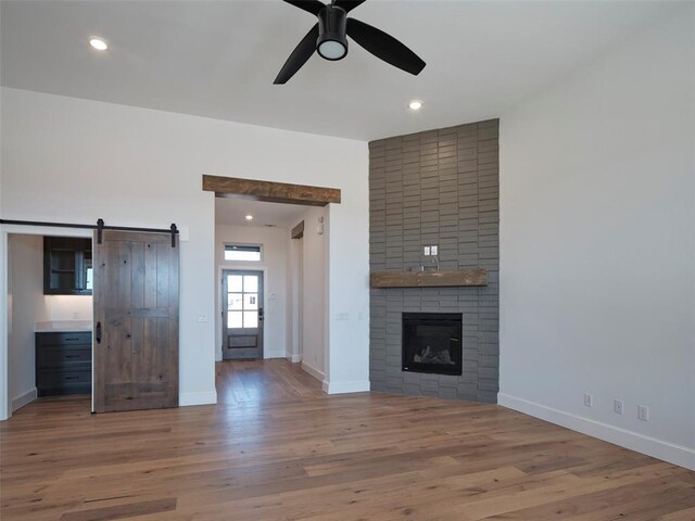 9116 SW 92nd St, Mustang, OK 73064 - unfurnished living room with a barn door, a ceiling fan, wood finished floors, a large fireplace, and baseboards