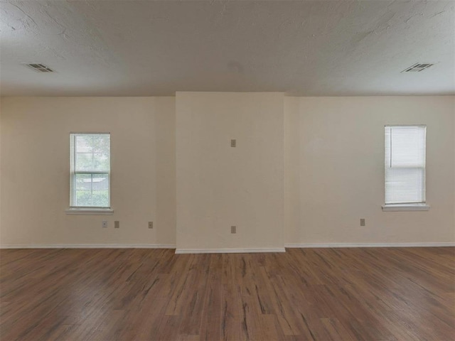 empty room with a textured ceiling, a wealth of natural light, and wood-type flooring