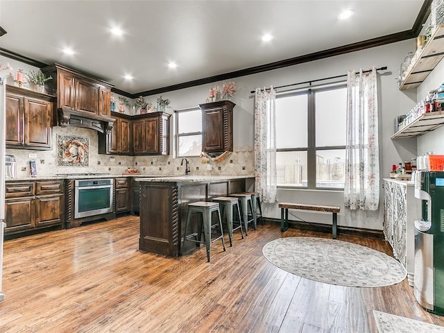 kitchen with a kitchen bar, light hardwood / wood-style floors, dark brown cabinets, crown molding, and appliances with stainless steel finishes