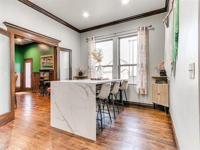 kitchen featuring wood-type flooring, a kitchen bar, and ornamental molding