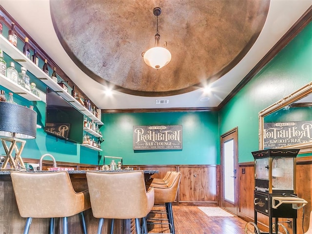 bar with a raised ceiling, wooden walls, hanging light fixtures, and hardwood / wood-style floors