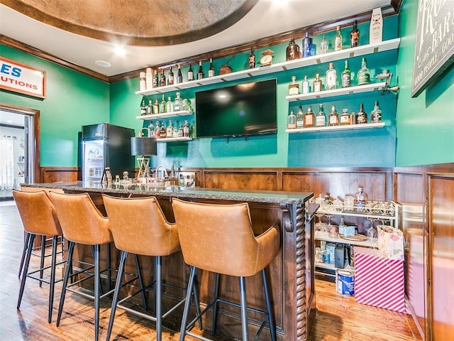 bar with black refrigerator, wood walls, and hardwood / wood-style flooring