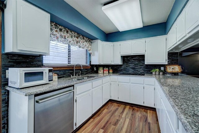 kitchen featuring backsplash, white microwave, a sink, and dishwasher