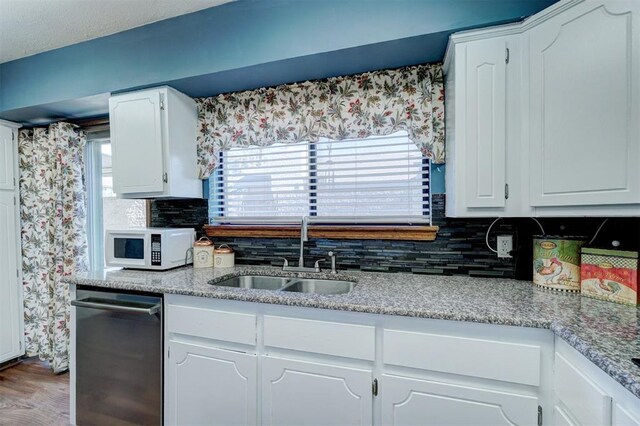 kitchen with backsplash, a sink, white microwave, dishwashing machine, and white cabinetry