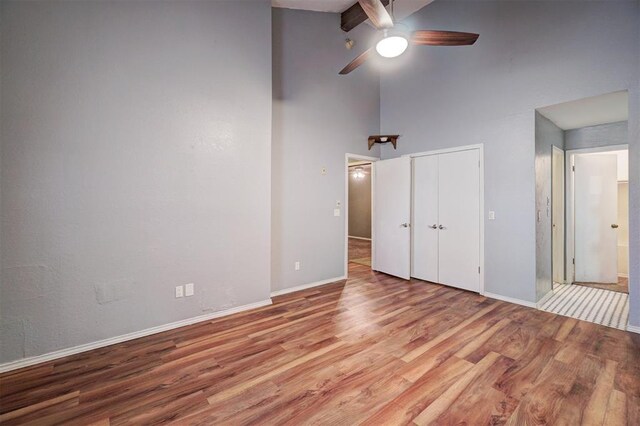 unfurnished bedroom with baseboards, high vaulted ceiling, wood finished floors, and a closet
