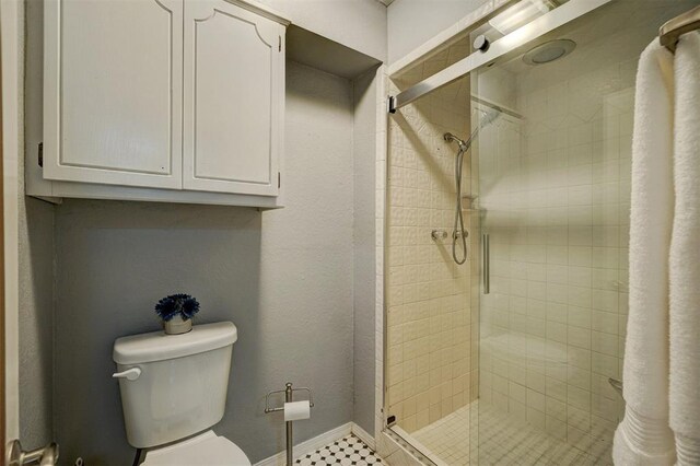 bathroom featuring toilet, baseboards, and a shower stall