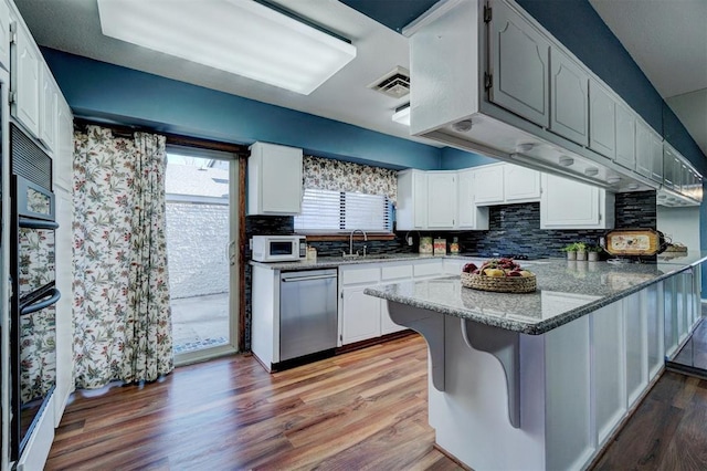kitchen with a peninsula, tasteful backsplash, a sink, light wood finished floors, and dishwasher