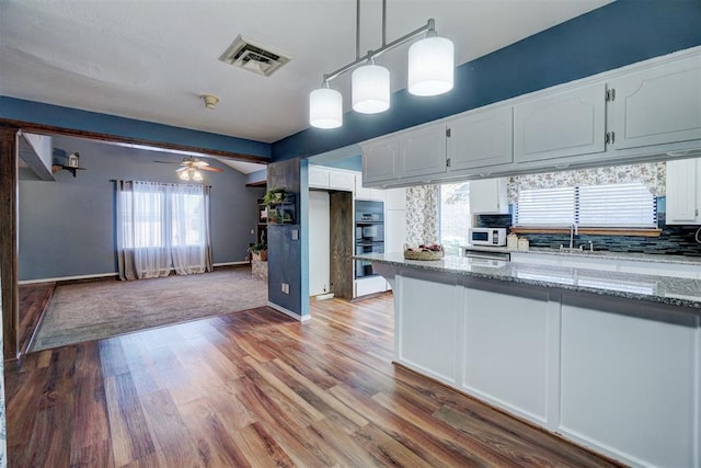 kitchen featuring white cabinetry, light stone countertops, visible vents, and white microwave