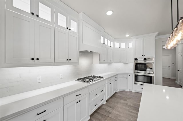 kitchen with decorative backsplash, stainless steel appliances, white cabinets, light countertops, and glass insert cabinets