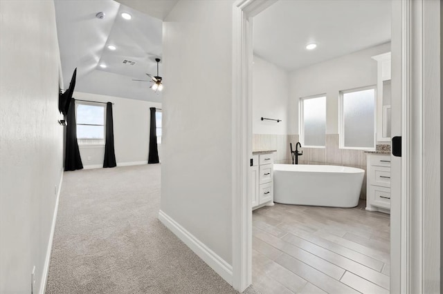 bathroom featuring a ceiling fan, a soaking tub, recessed lighting, vaulted ceiling, and wainscoting