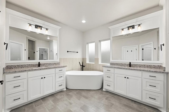 full bath with a sink, a wainscoted wall, a freestanding bath, and two vanities