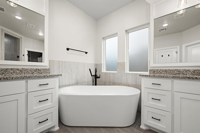 full bath with visible vents, a freestanding bath, and two vanities