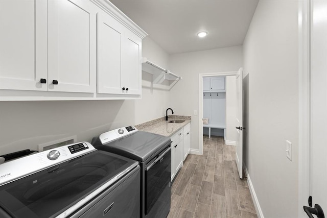 laundry room featuring a sink, cabinet space, separate washer and dryer, light wood finished floors, and baseboards