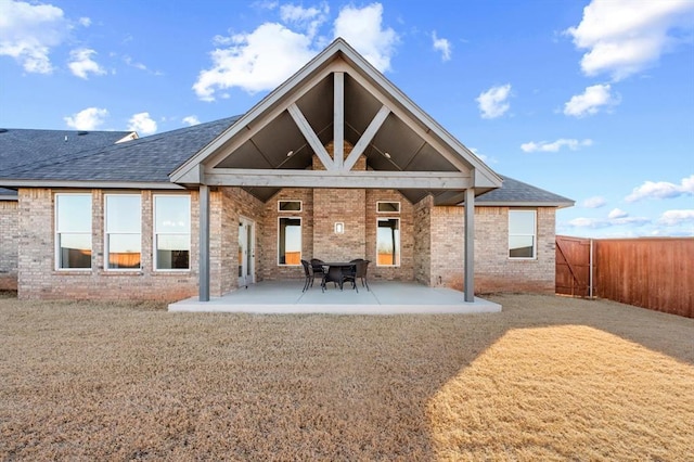 back of house with brick siding, a shingled roof, a patio, and fence