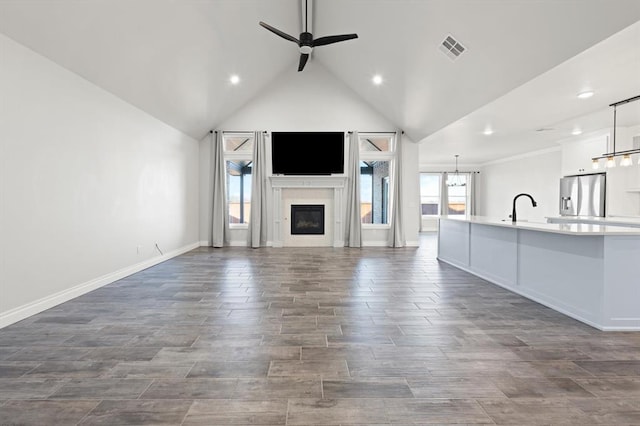 unfurnished living room featuring visible vents, ceiling fan with notable chandelier, a glass covered fireplace, dark wood finished floors, and lofted ceiling