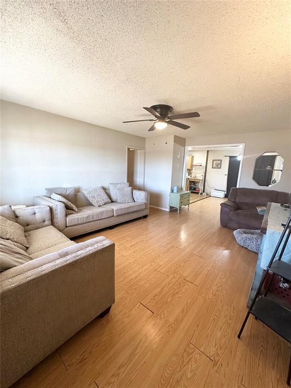 living room featuring a textured ceiling, wood-type flooring, and ceiling fan