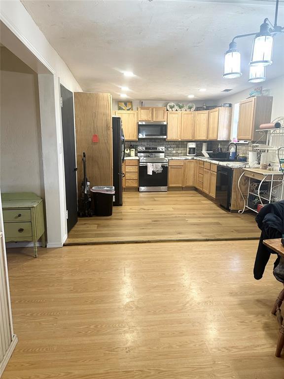 kitchen with sink, tasteful backsplash, decorative light fixtures, light hardwood / wood-style flooring, and stainless steel appliances