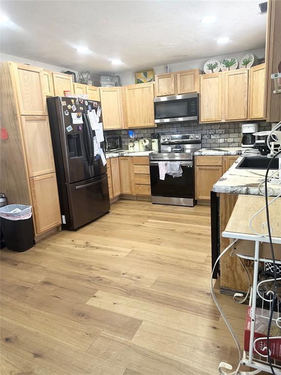 kitchen featuring light brown cabinetry, sink, light wood-type flooring, and appliances with stainless steel finishes