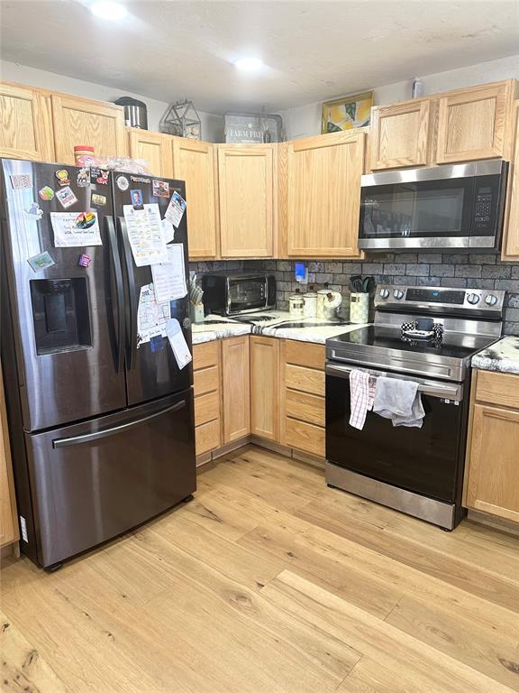 kitchen with appliances with stainless steel finishes, light brown cabinets, light hardwood / wood-style floors, and decorative backsplash