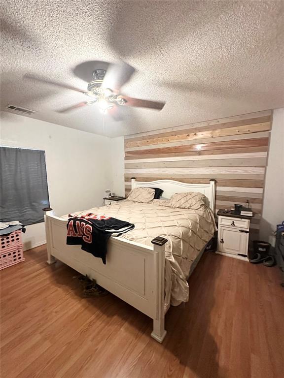 bedroom with hardwood / wood-style floors, a textured ceiling, wooden walls, and ceiling fan