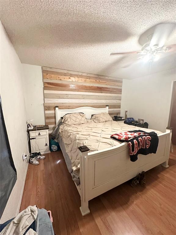 bedroom featuring hardwood / wood-style floors, a textured ceiling, ceiling fan, and wood walls