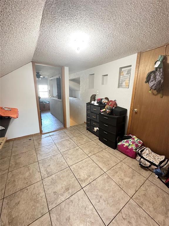 unfurnished bedroom featuring lofted ceiling, a textured ceiling, and light tile patterned floors