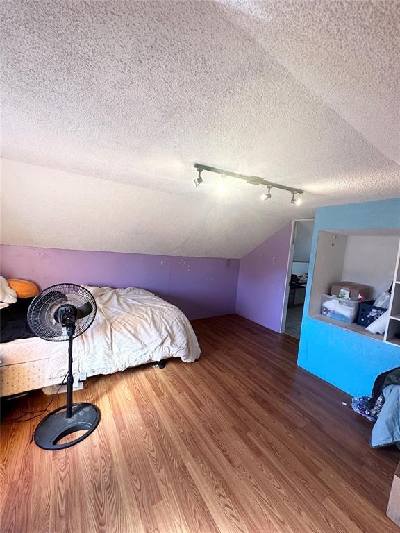 bedroom with lofted ceiling, hardwood / wood-style floors, and a textured ceiling